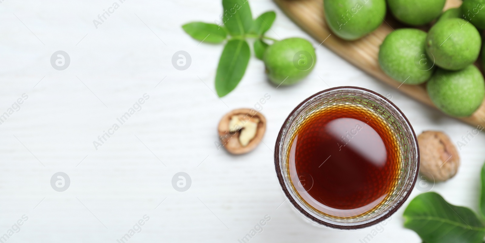 Image of Delicious liqueur and fresh walnuts on white wooden table, flat lay with space for text. Banner design