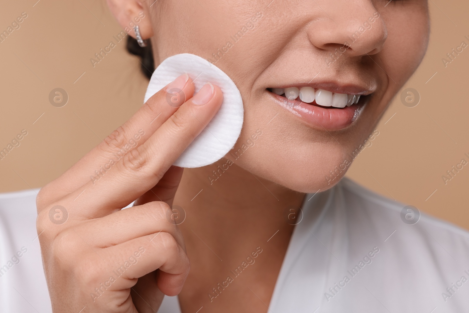 Photo of Young woman cleaning her face with cotton pad on beige background, closeup