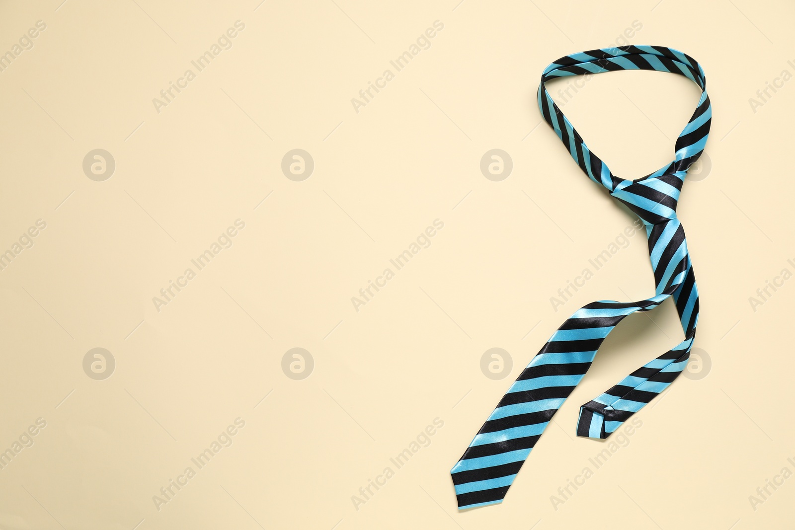 Photo of Striped necktie on beige background, top view. Space for text