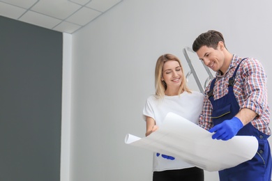 Photo of Male decorator and young woman studying repair plan indoors