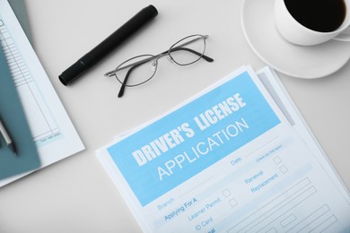 Photo of Driver's license application form, glasses and cup of coffee on white table, above view