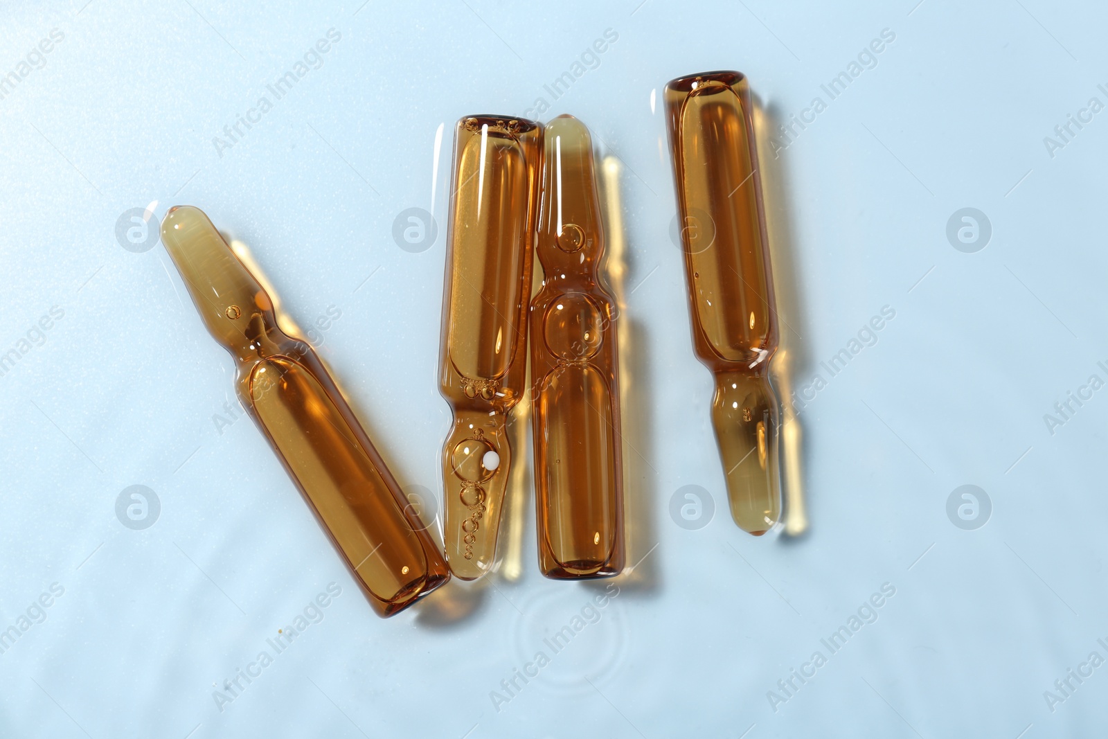 Photo of Skincare ampoules in water on light blue background, top view