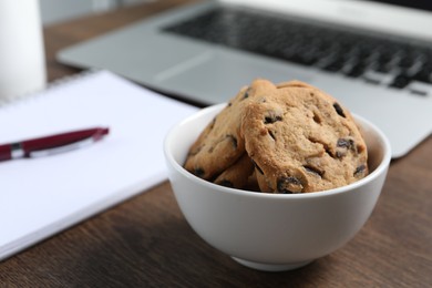 Photo of Bowl with chocolate chip cookies on wooden table in office, closeup. Space for text
