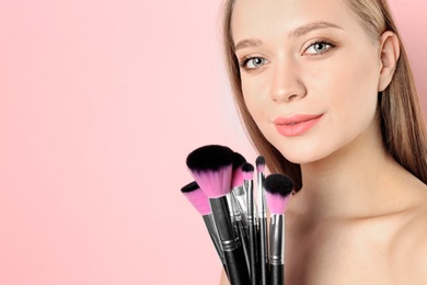 Photo of Portrait of beautiful young woman with makeup brushes on color background. Space for text