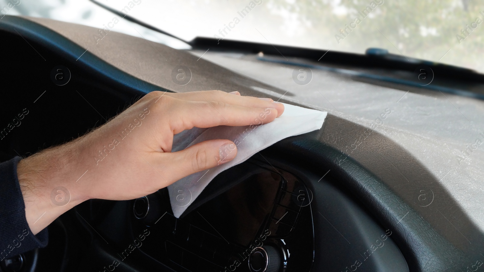 Photo of Man cleaning dashboard with wet wipe in car, closeup. Protective measures