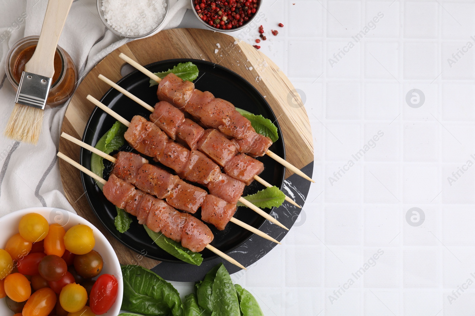 Photo of Wooden skewers with cut raw marinated meat on white tiled table, flat lay. Space for text