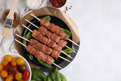Photo of Wooden skewers with cut raw marinated meat on white tiled table, flat lay. Space for text