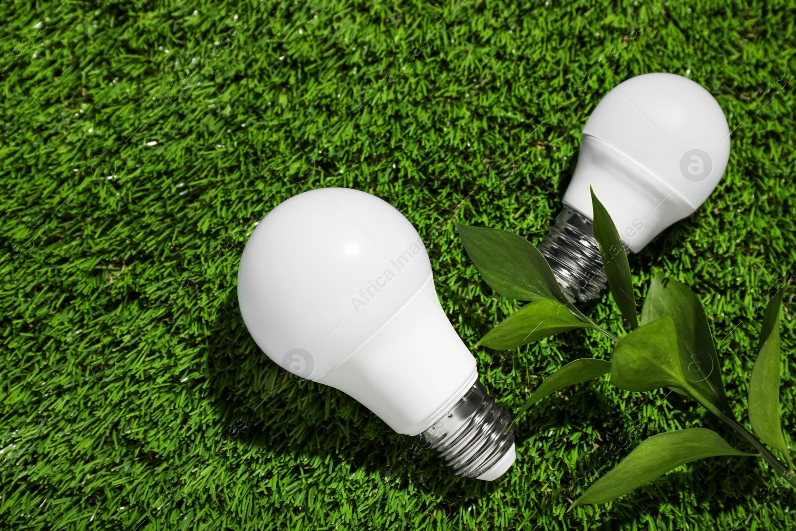 Photo of New light bulbs on fresh green grass, flat lay