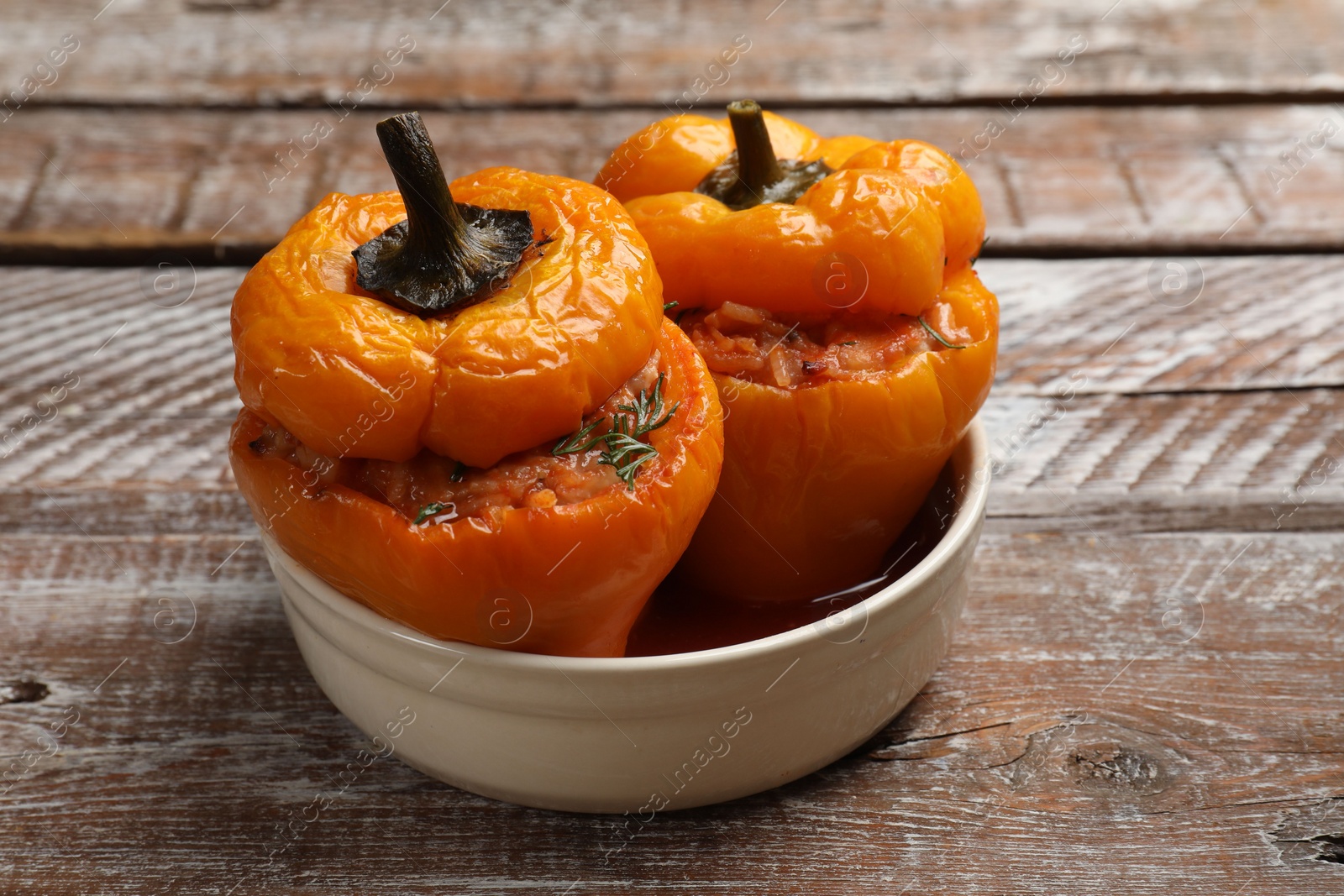 Photo of Tasty stuffed peppers in bowl on wooden rustic table, closeup