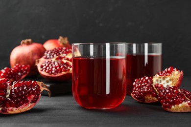 Photo of Tasty pomegranate juice in glasses and fresh fruits on black wooden table