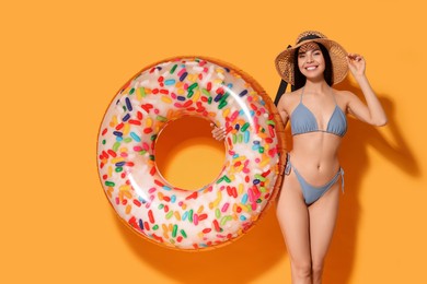 Photo of Young woman with straw hat holding inflatable ring against orange background