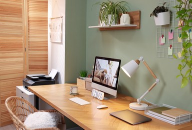 Photo of Stylish workplace with computer, laptop and lamp near olive wall at home