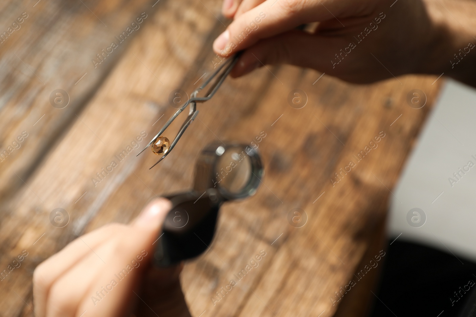 Photo of Male jeweler evaluating precious gemstone at table in workshop, closeup