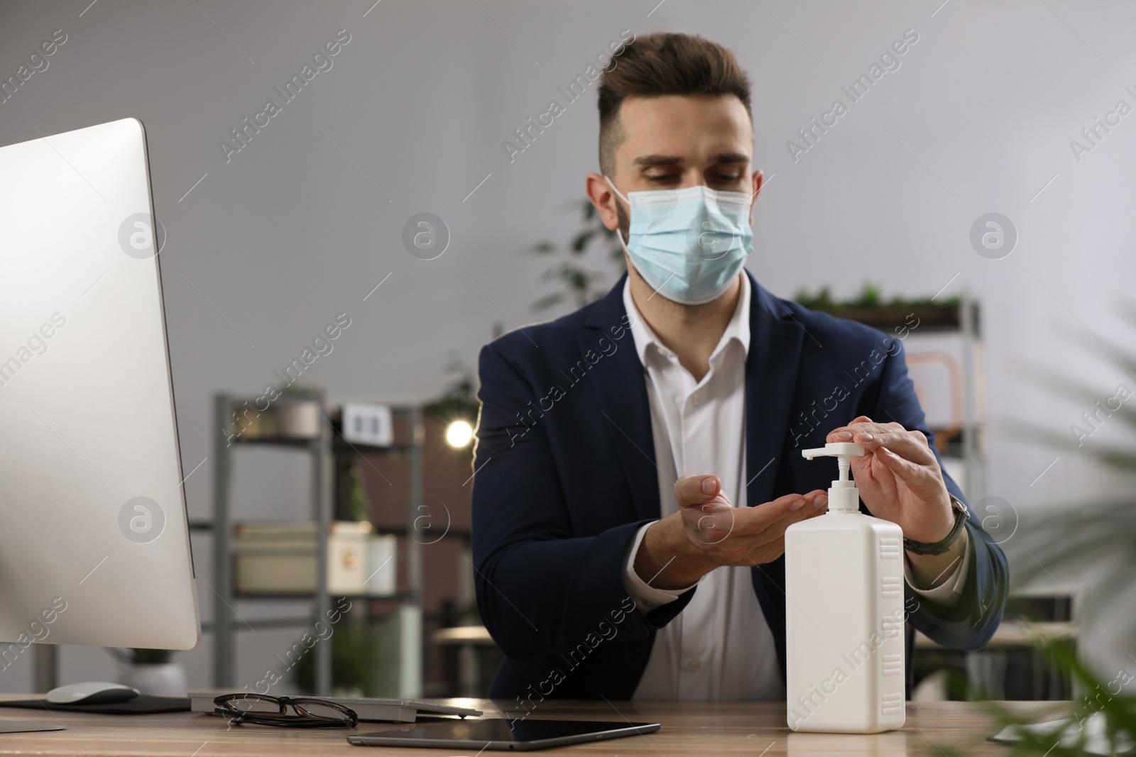 Photo of Man applying sanitizer in office, focus on hands. Personal hygiene during Coronavirus pandemic