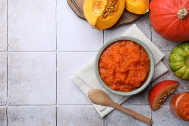 Bowl of delicious pumpkin jam and fresh pumpkins on tiled surface, flat lay. Space for text