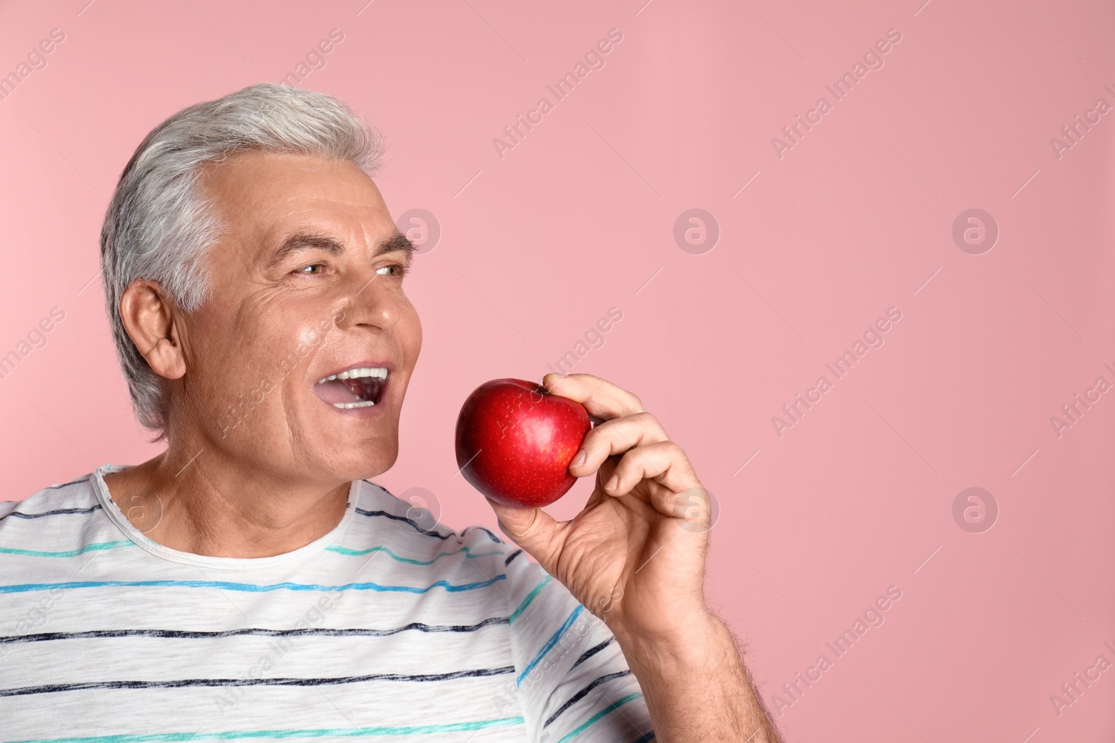 Photo of Mature man with healthy teeth and apple on color background. Space for text