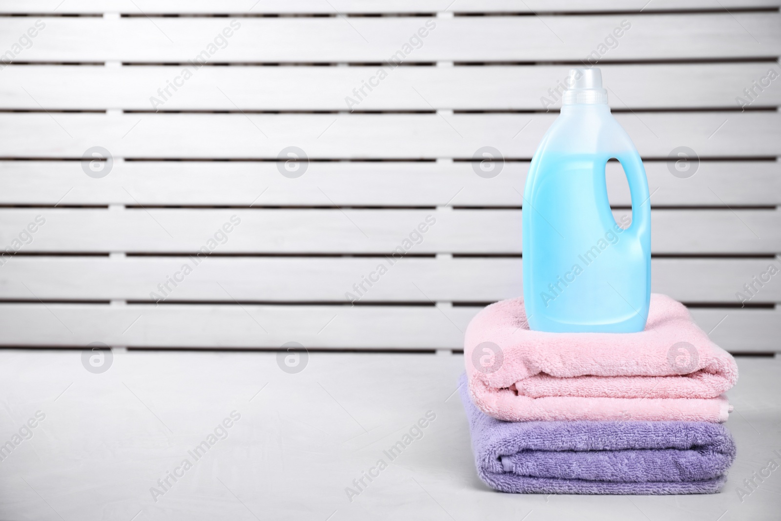 Photo of Clean towels and bottle of laundry detergent on table against blurred background. Space for text