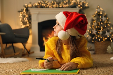 Cute child writing letter to Santa Claus while lying on floor at home. Christmas celebration