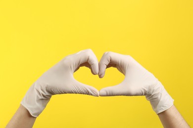 Photo of Person in medical gloves showing heart gesture on yellow background, closeup of hands