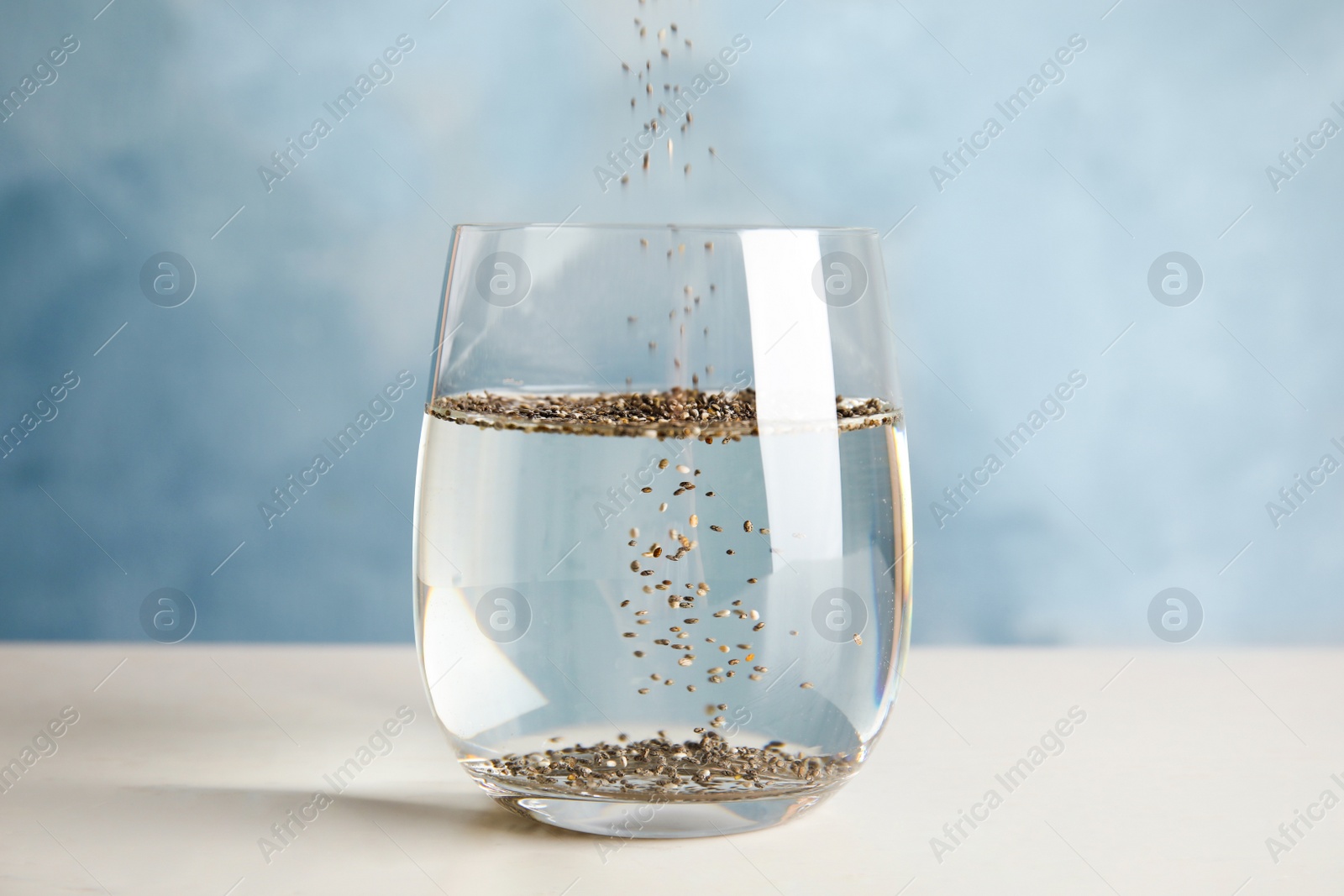 Photo of Pouring chia seeds into glass with water on table