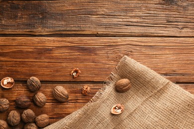Photo of Burlap fabric and walnuts on wooden table, top view. Space for text