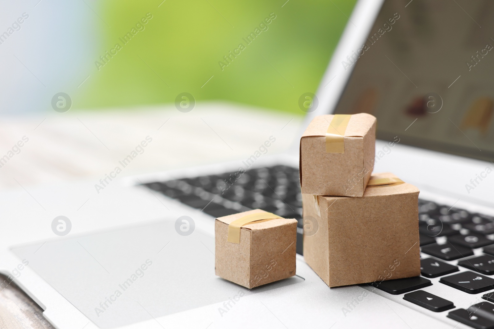 Photo of Internet shopping. Small cardboard boxes and laptop on table, closeup. Space for text