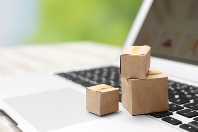 Internet shopping. Small cardboard boxes and laptop on table, closeup. Space for text