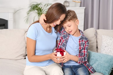 Little boy presenting his mother with gift on sofa at home