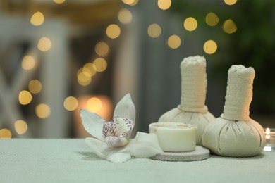 Photo of Spa composition. Herbal massage bags, soap bar and orchid flower on white towel against blurred lights, space for text