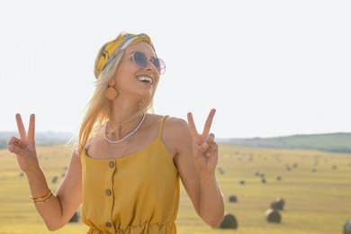 Photo of Beautiful hippie woman showing peace signs in field, space for text