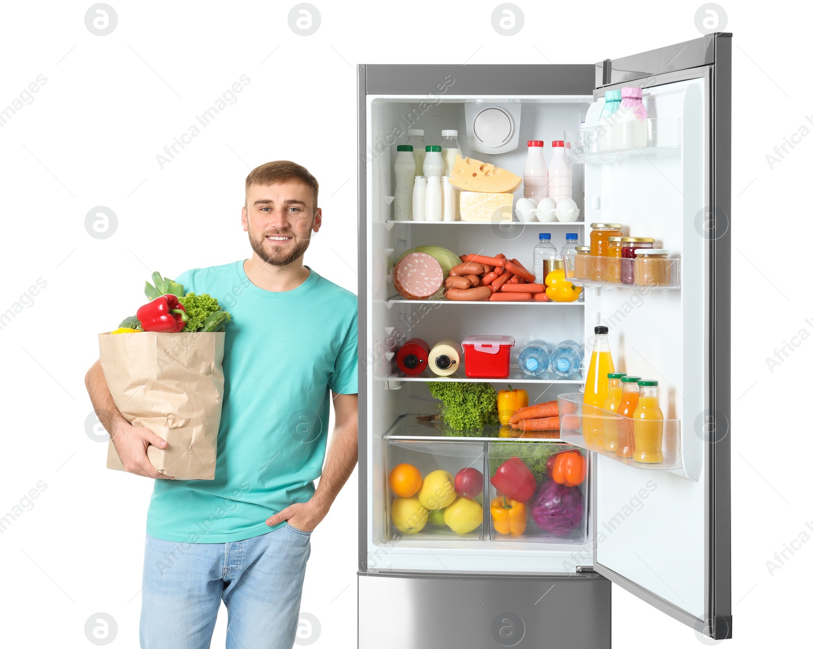 Photo of Young man with bag of groceries near open refrigerator on white background