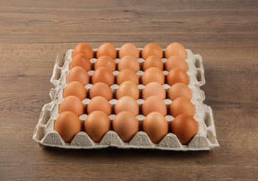 Raw chicken eggs in carton tray on wooden table
