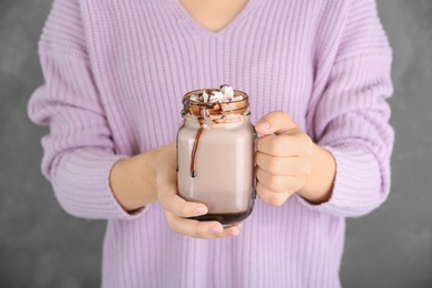 Photo of Woman holding jar with chocolate milk and marshmallows on grey background