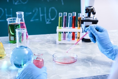 Scientist taking sample of liquid with dropper at table against chalkboard, closeup. Chemistry glassware