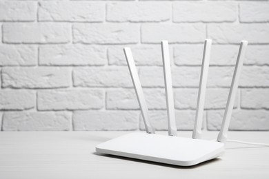 Photo of New Wi-Fi router on white wooden table against brick wall. Space for text