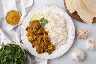 Photo of Delicious chicken curry with rice and ingredients on white tiled table, flat lay