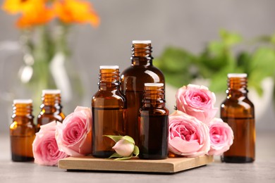 Bottles with essential oil and roses on light table, closeup