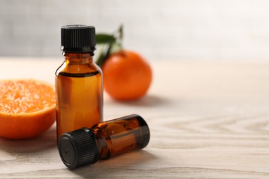 Photo of Bottles of tangerine essential oil and fresh fruits on wooden table, closeup. Space for text