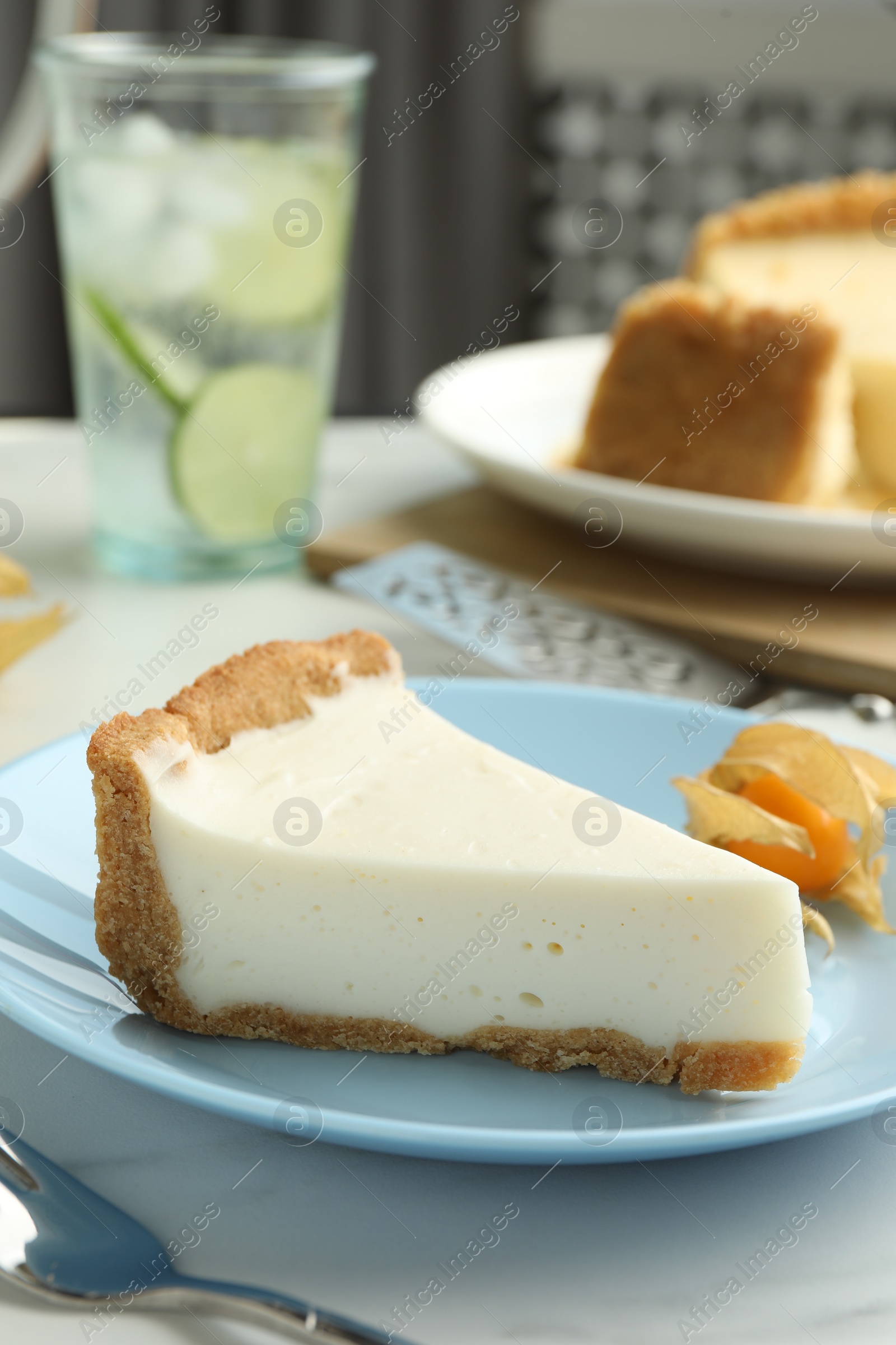 Photo of Piece of tasty vegan tofu cheesecake and physalis fruit on white table, closeup