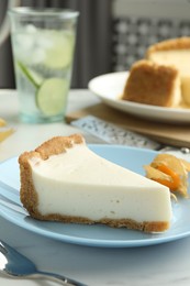 Piece of tasty vegan tofu cheesecake and physalis fruit on white table, closeup