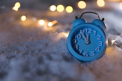 Photo of Alarm clock and Christmas lights on white snow outdoors, space for text. Midnight countdown