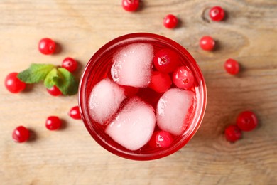 Tasty cranberry juice with ice cubes in glass and fresh berries on wooden table, top view