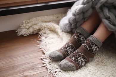 Photo of Woman wearing knitted socks on window sill indoors, closeup. Warm clothes