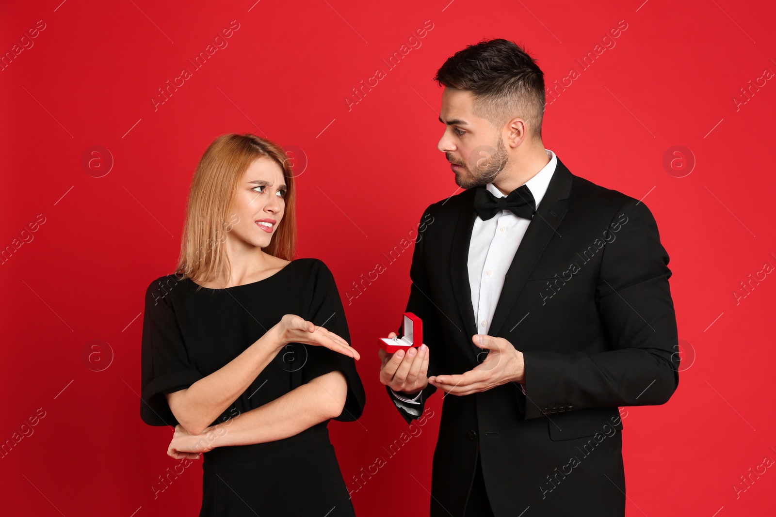 Photo of Young woman rejecting engagement ring from boyfriend on red background