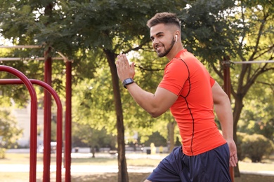 Photo of Young man with wireless headphones listening to music while exercising on sports ground. Space for text