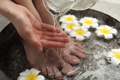 Photo of Woman pouring water onto hand while soaking her feet in bowl, closeup. Spa treatment