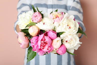 Woman with bouquet of beautiful peonies on beige background, closeup