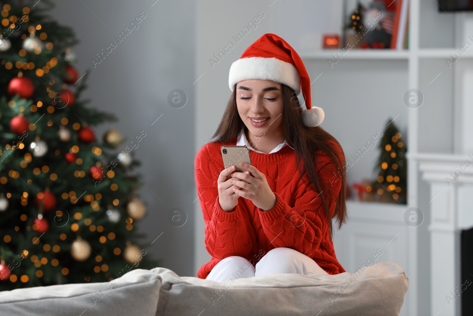 Photo of Smiling woman wearing red Christmas hat with smartphone in cosy room
