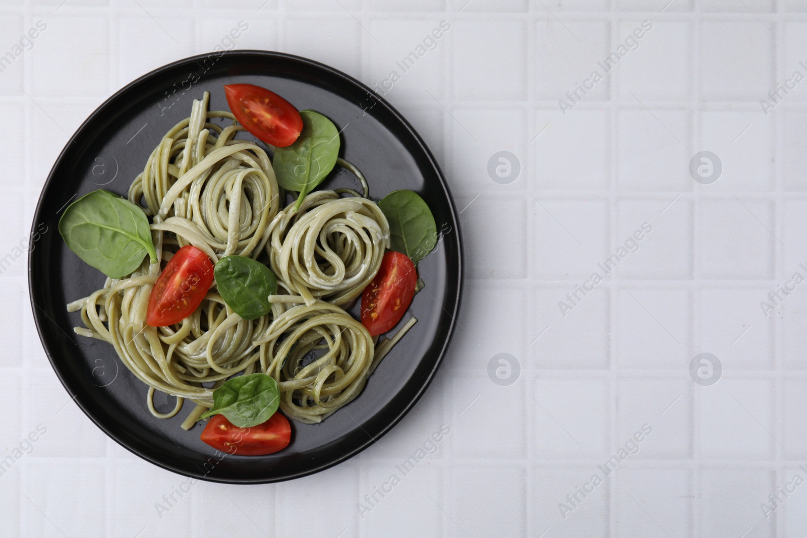 Photo of Tasty pasta with spinach, sauce and tomatoes on white tiled table, top view. Space for text