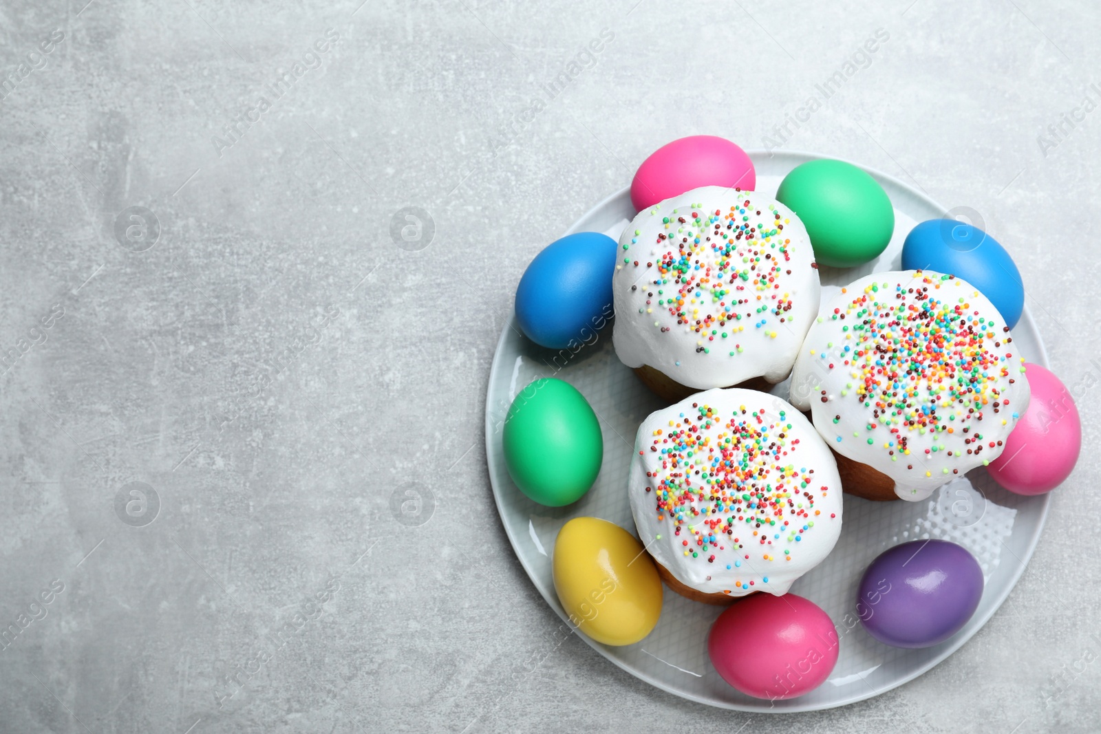 Photo of Easter cakes and colorful eggs on light grey table, top view